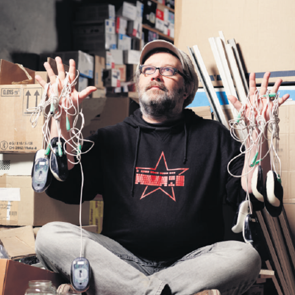 Bernd Fix, sitting on the ground, mouse cables weaved through his fingers with nine mice hanging from them.